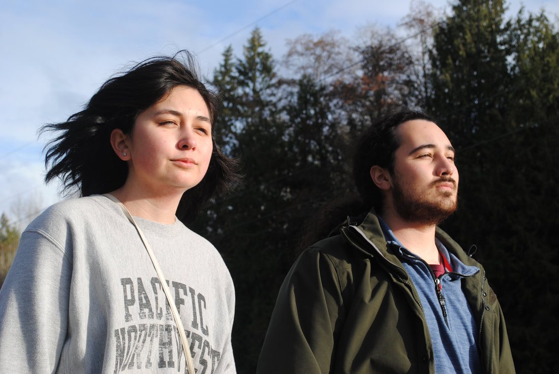 Two people facing the horizon in a wooded clearing